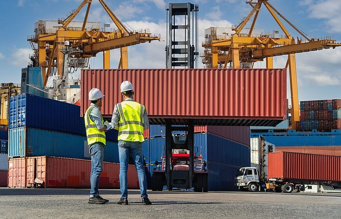 Deux responsables en gilet de sécurité devant un conteneur soulevé sur un terminal